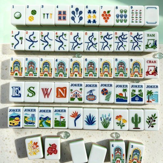 Neat full layout of Tropical Golf Resort American mahjong tiles, mint green tile backs, pink-green striped sides, custom golf, palm tree and resort building illustrations, arranged on light speckled countertop