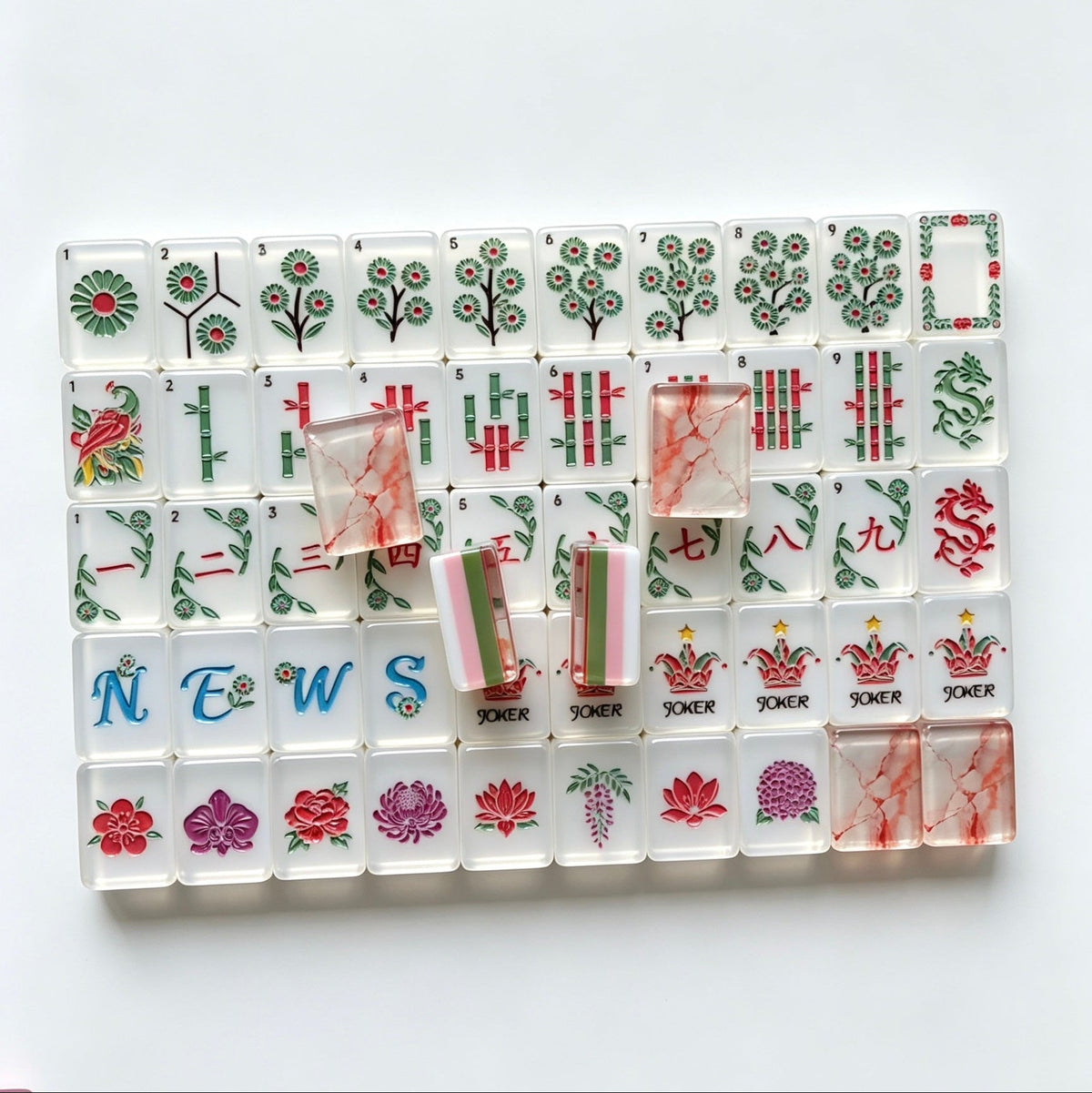 Flat lay of Pink Marble Floral American mahjong tiles arranged neatly on clean white background, white tile fronts with green floral dot patterns, classic bamboo, red dragons, multi-color flower tiles and crown jokers