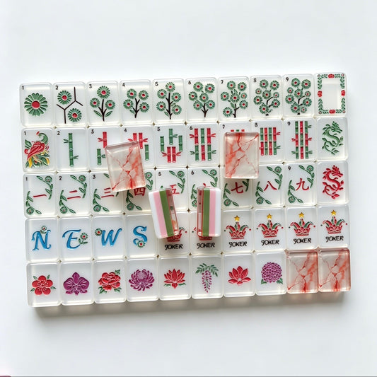 Flat lay of Pink Marble Floral American mahjong tiles arranged neatly on clean white background, white tile fronts with green floral dot patterns, classic bamboo, red dragons, multi-color flower tiles and crown jokers