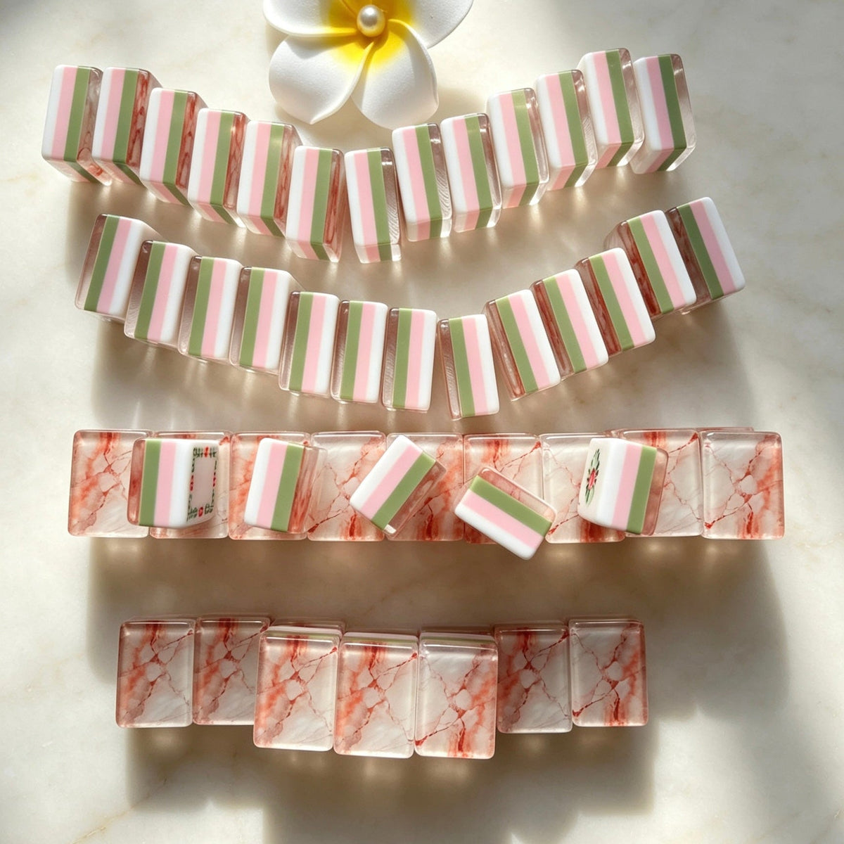 Flat lay of Pink Marble Floral American mahjong tiles arranged neatly on clean white background, white tile fronts with green floral dot patterns, classic bamboo, red dragons, multi-color flower tiles and crown jokers