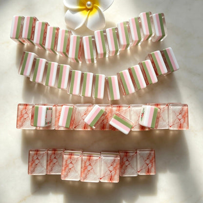 Flat lay of Pink Marble Floral American mahjong tiles arranged neatly on clean white background, white tile fronts with green floral dot patterns, classic bamboo, red dragons, multi-color flower tiles and crown jokers
