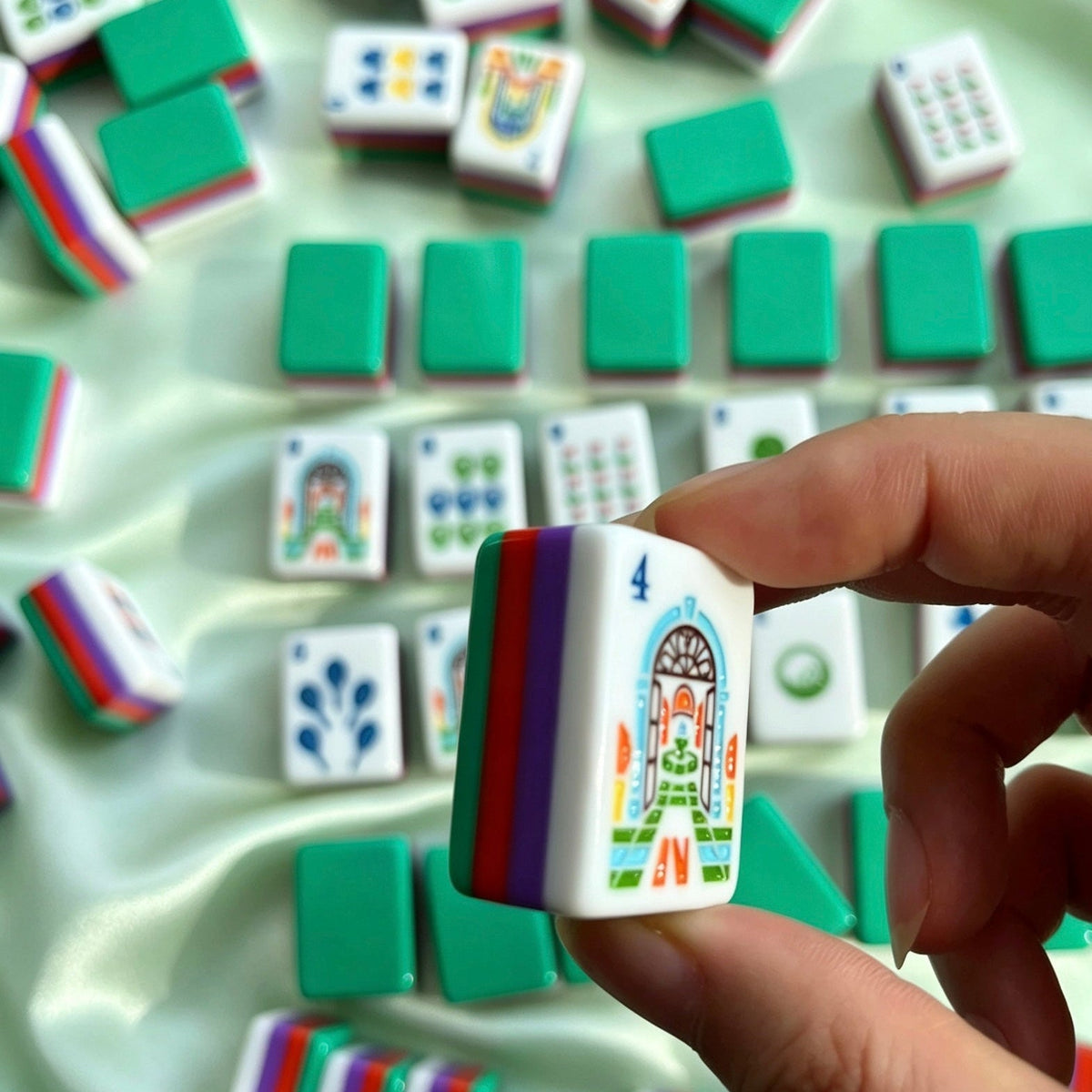 Scattered tropical golf resort mahjong tiles on textured off-white countertop, deep green backs and rainbow striped edges, golf and resort custom illustrations