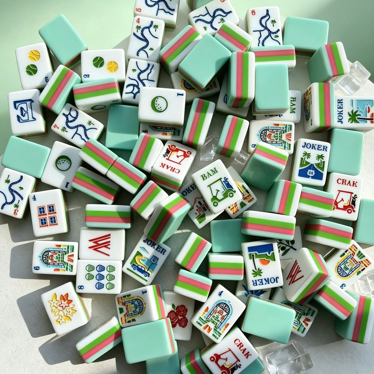 Overhead shot of scattered tropical golf resort mahjong tiles, mint green backs, pink and green striped edges, vacation themed artwork on white tile faces, styled on light green background