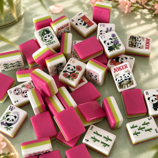 Close-up of four Panda Blossom mahjong tiles standing upright, showing white, lime green and fuchsia layered side stripes, styled on green ceramic plate with cherry blossoms and bamboo in background