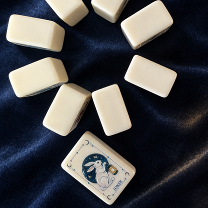 Top-down view of mixed Moon Rabbit Tarot mahjong tiles, cream ivory tiles with tarot card frame, moon and star motifs, wildflower, ocean wave and rabbit joker illustrations
